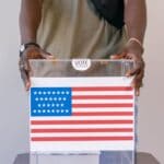 Corinth Mayoral Race: Absentee Voting Steady Before Oct. 13 A voter places a ballot in a clear ballot box, illustrating the Corinth mayoral race