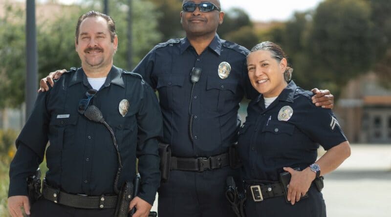 Group of uniformed police officers smiling together outdoors, illustrating Corinth police officers mentoring students