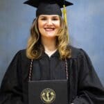 Presley McMillan’s NEMCC path leads from HSE to daycare work A woman in a black graduation cap and gown smiles while holding a diploma cover in front of a plain blue backdrop.