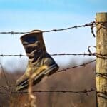 The 5 Best Work Boots for Farm and Property Work in Alcorn County A worn brown leather work boot hanging on a barbed-wire fence on a farm