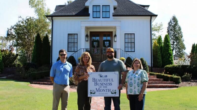 Four people hold a Beautiful Business of the Month sign in front of The Carriage House in Corinth