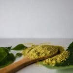 Corinth Kratom Ban Takes Effect Immediately Herbal powder on a wooden spoon with green leaves, illustrating products covered by the Corinth kratom ban