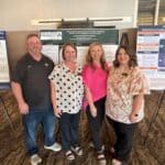 NEMCC, Delta State nursing students present projects at Destin conference Four people stand in front of conference poster presentations in a meeting room.