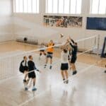 Players go up for the ball at the net during an indoor volleyball match, illustrating the NEMCC volleyball sweep
