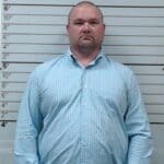 State Auditor announces arrests in Guntown fraud case A man stands in front of a height chart in a booking-style photo.