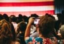 Trump Rally in Corinth Confirmed for Oct. 26; RSVP Required Crowd photographing an American flag at an indoor rally, illustrating the Trump rally in Corinth