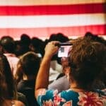 Trump Rally in Corinth Confirmed for Oct. 26; RSVP Required Crowd photographing an American flag at an indoor rally, illustrating the Trump rally in Corinth