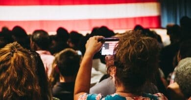 Trump Rally in Corinth Confirmed for Oct. 26; RSVP Required Crowd photographing an American flag at an indoor rally, illustrating the Trump rally in Corinth